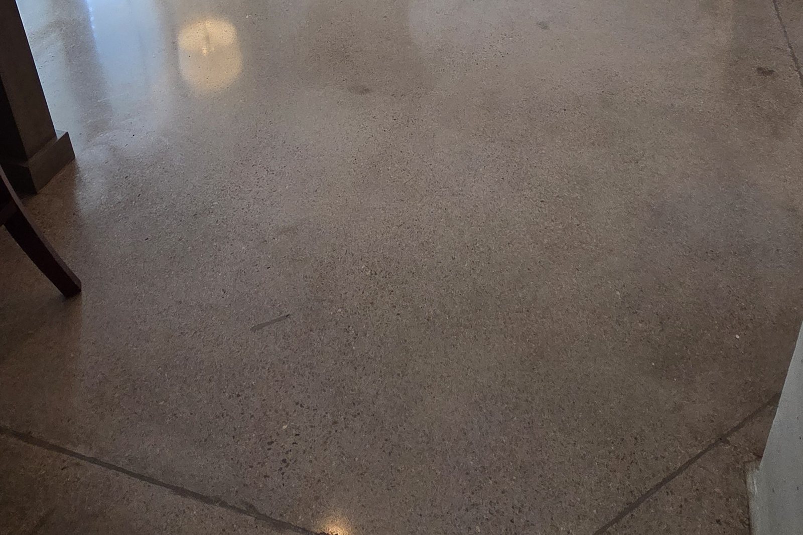 Close view of a residential polished concrete floor showing natural aggregate, saw-cut control joints, and a reflective finish