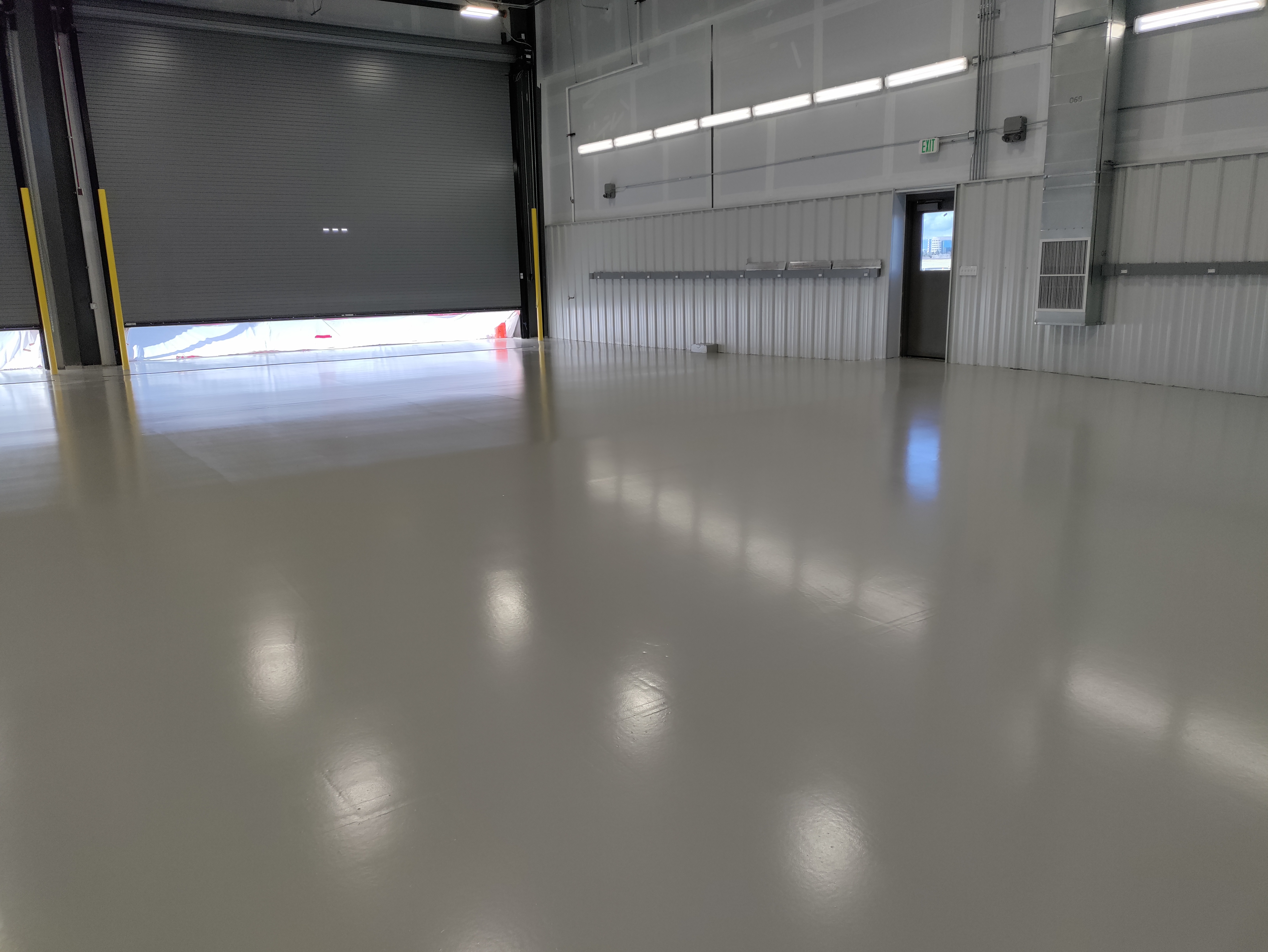 Industrial warehouse epoxy floor with roll-up door and safety bollards — warehouse epoxy coating Colorado