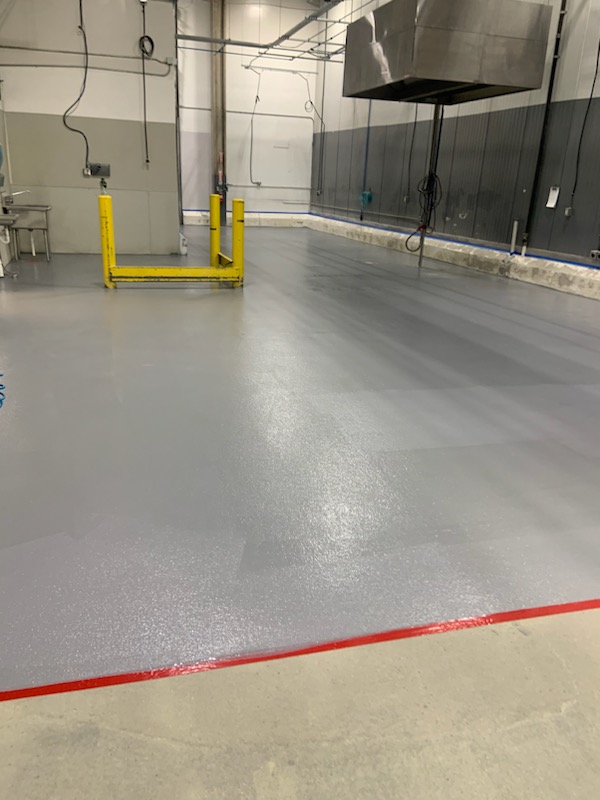 Gray traffic coating with red safety line and yellow bollards in industrial facility — traffic coatings Denver CO