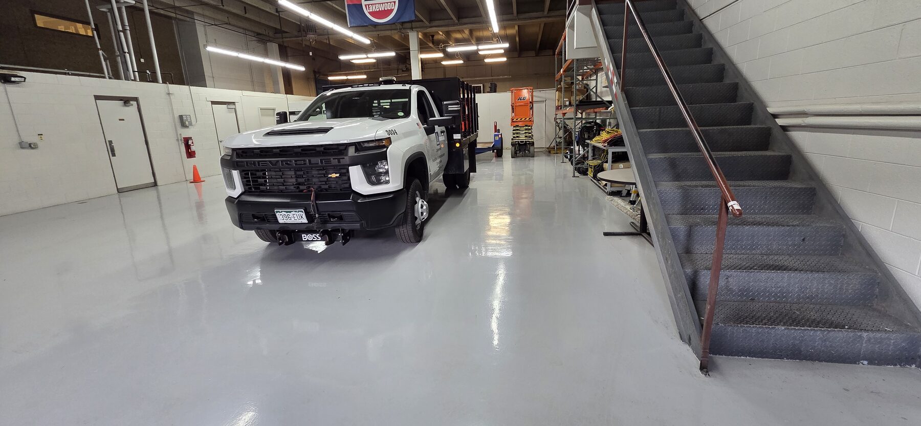 Glossy gray traffic coating in equipment bay beside steel stairs with work truck — traffic coating contractor Colorado