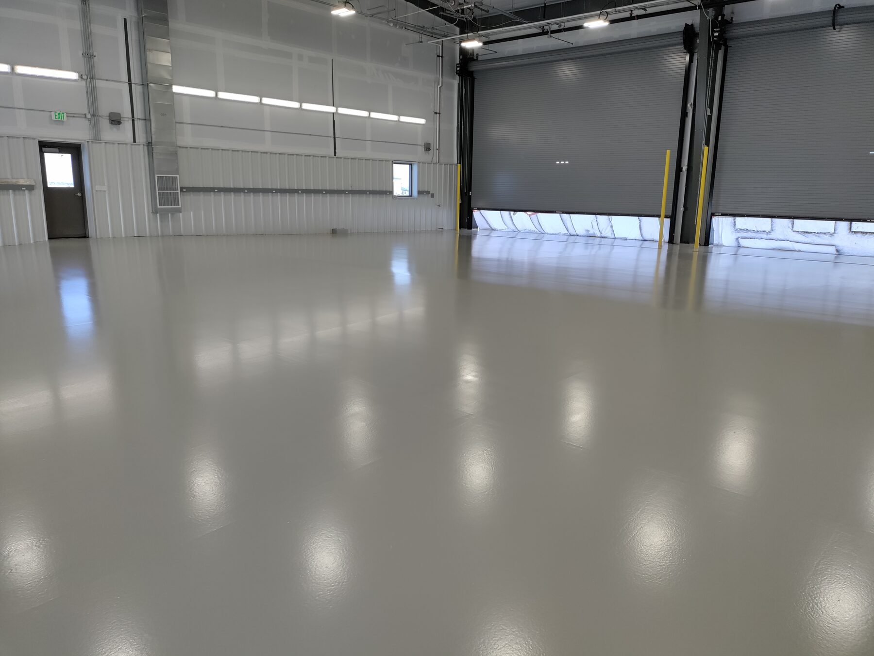 Freshly applied light gray traffic coating in empty warehouse bay with roll-up doors — traffic coatings Denver CO